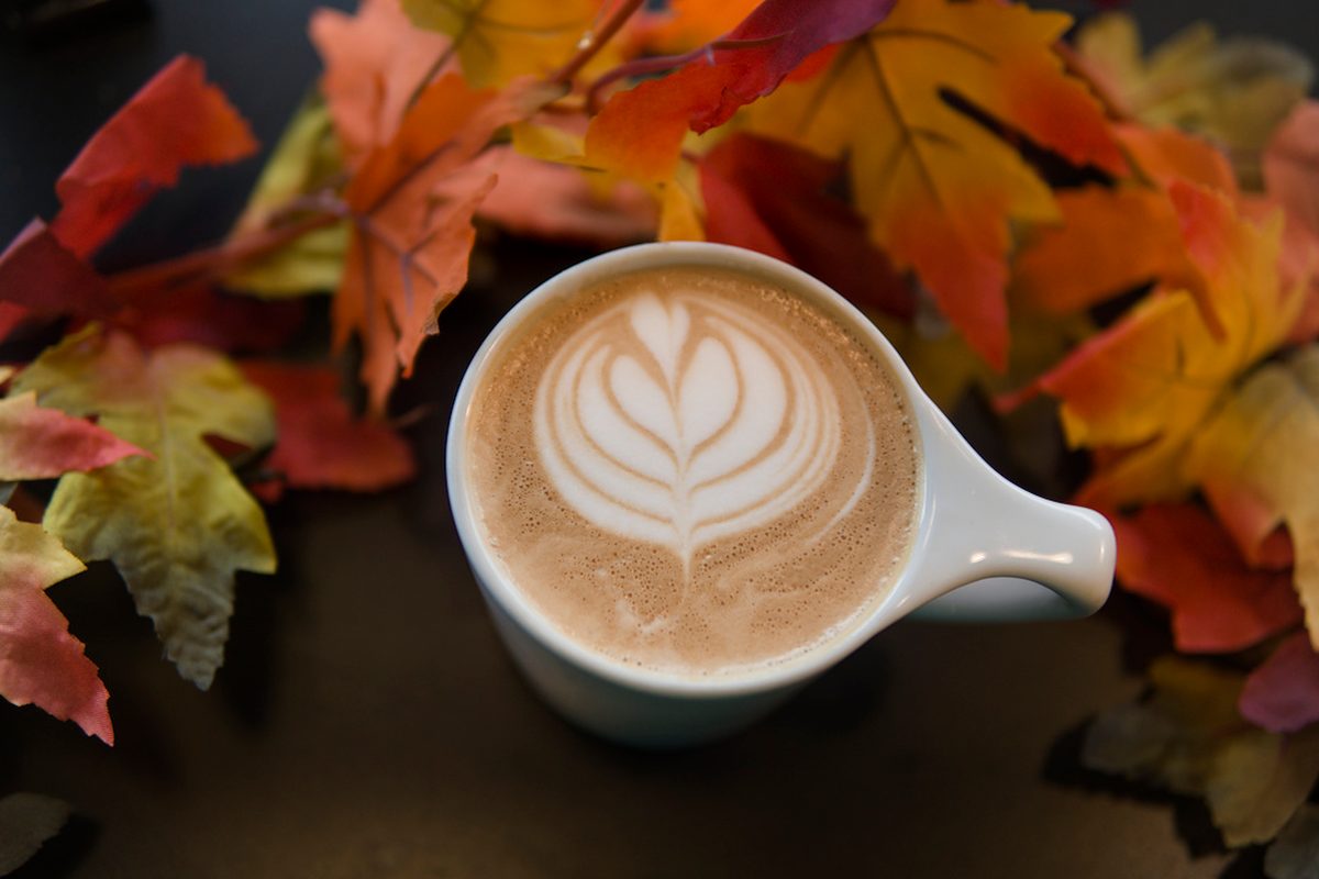 Latte with leaf-shaped foam art surrounded by autumn leaves